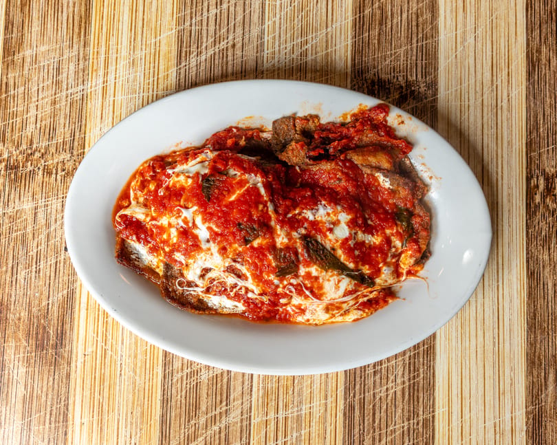 A white oval plate holds a dish of meat covered in red sauce and melted white cheese.