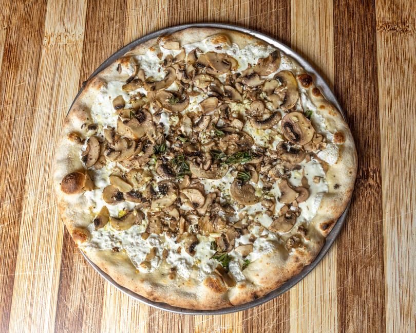 White pizza with mushrooms, ricotta cheese, garlic, and herbs on a wooden table.
