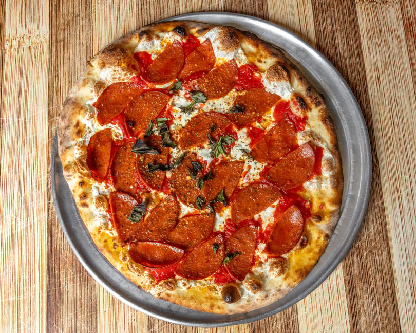 Pepperoni pizza with dollops of ricotta cheese and fresh basil on a metal pan.