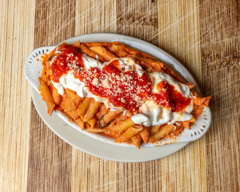 Baked penne pasta with red sauce, melted mozzarella, and grated parmesan cheese in a white dish.